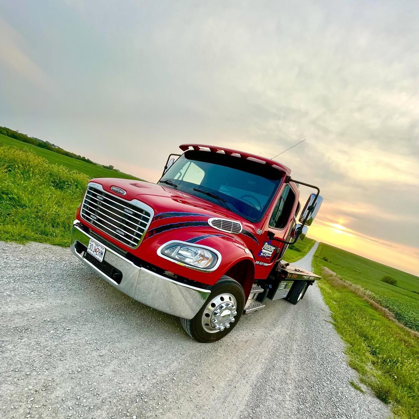 Red Freightliner M2 flatbed number 106 on a gravel road at sunset