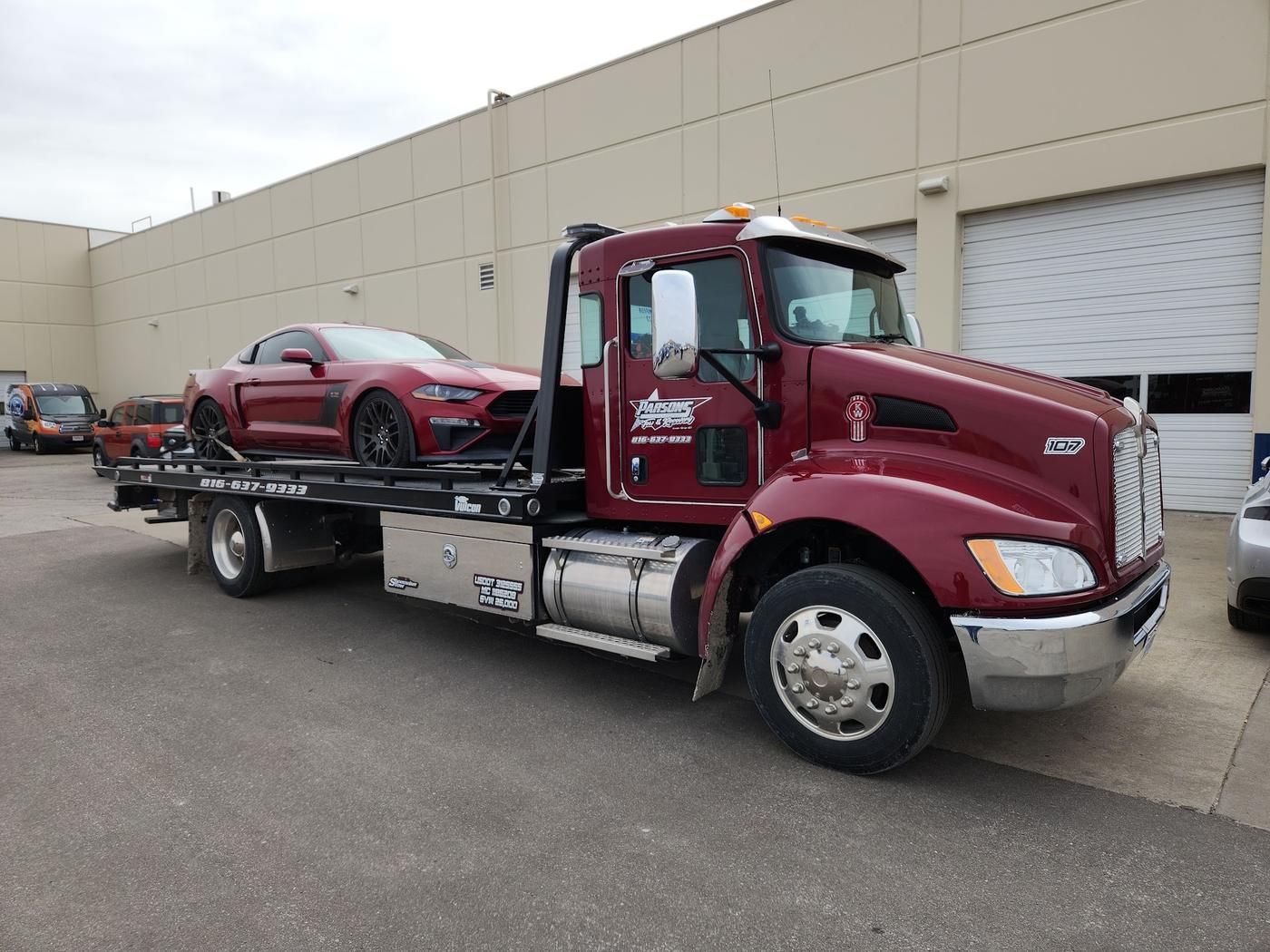 Parsons flatbed loaded with a red Mustang outside a body shop