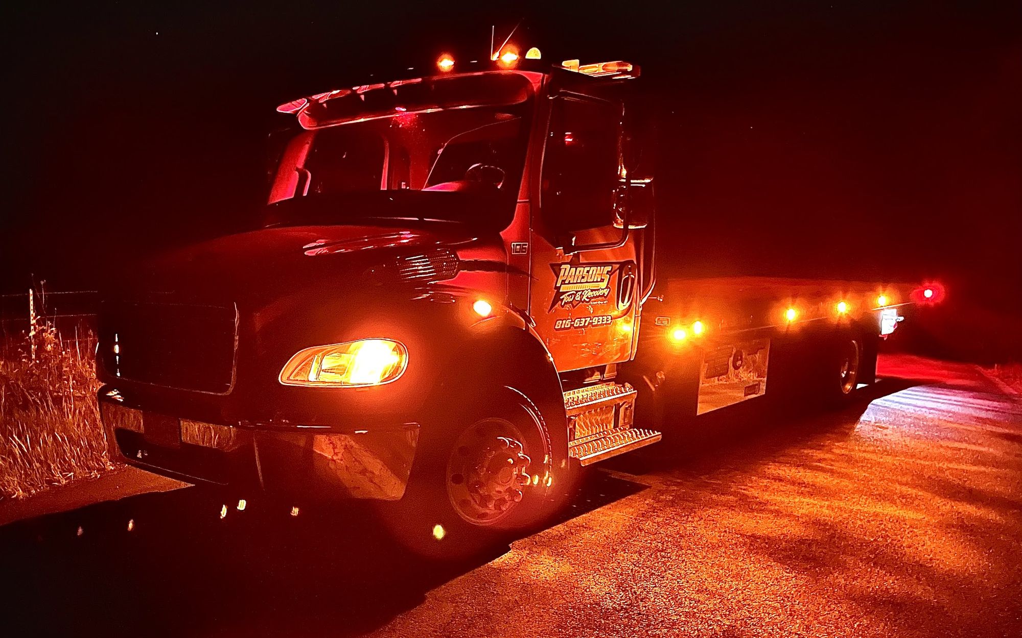Parsons flatbed tow truck lit amber at night on the roadside