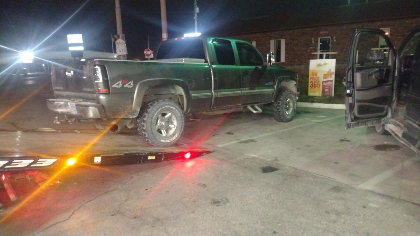 Green Chevy 4x4 being winched onto the Parsons flatbed at a gas station at night